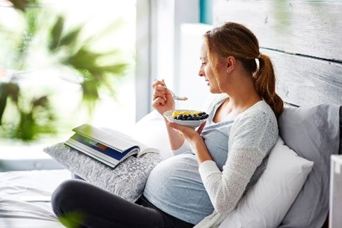 Mujer en embarazo comiendo un plato de frutas