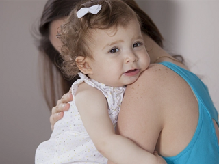 Imagen de una madre sosteniendo a su bebé en sus hombros, mientras la bebé muestra una expresión de dolor debido a padecer apendicitis
