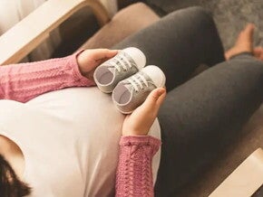 Mamá embarazada de un bebé arcoíris cogiendo unos zapatitos.