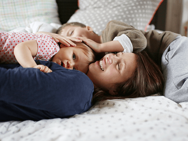 Estrategias efectivas para fomentar la autoestima de tus hijos Una mujer y dos niños felices acostados en una cama.