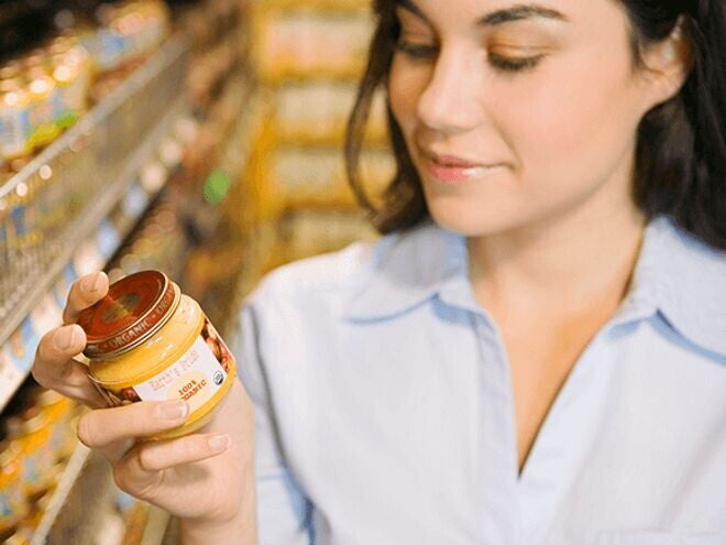 Aprende a leer las etiquetas nutricionales Mujer leyendo etiqueta nutricional con un frasco de colado para bebes