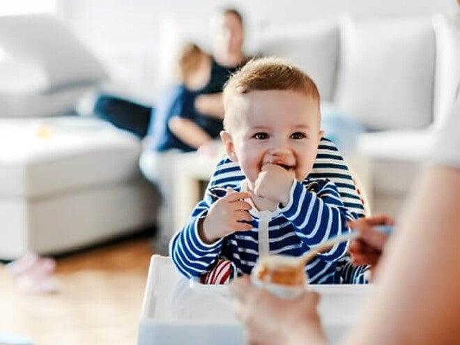 Bebé en su silla comiendo alimentos sólidos