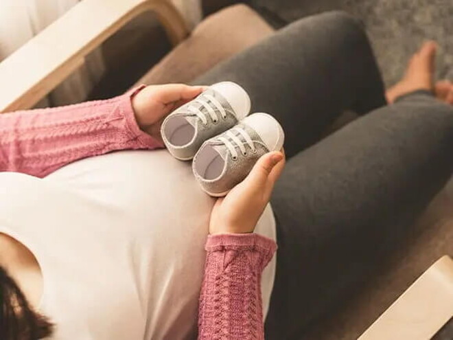 Mamá embarazada de un bebé arcoíris cogiendo unos zapatitos.