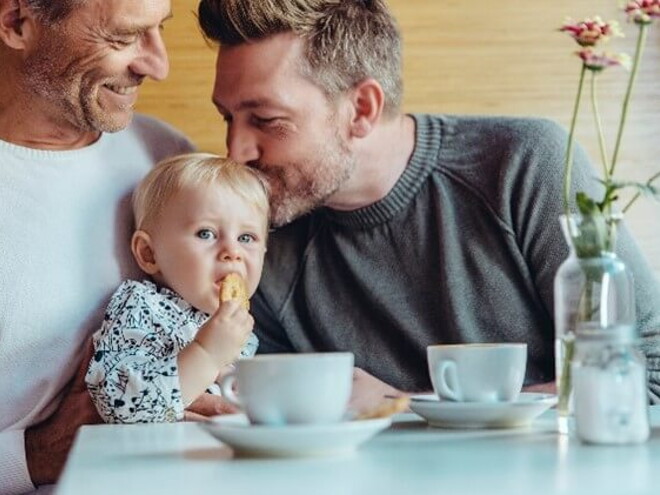 Conoce cuándo puedes darle galletas para bebés a tu hijo. Niña comiendo galletas para bebés con su papá y abuelo.