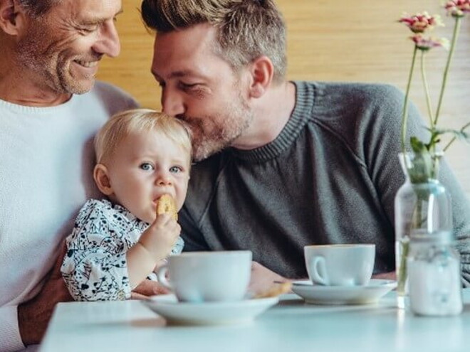 Niña comiendo galletas para bebés con su papá y abuelo.