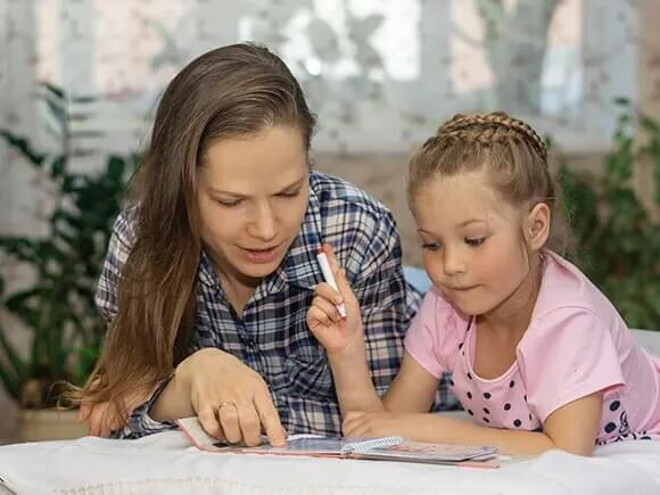 Mamá explicando a su hija por medio de un libro.