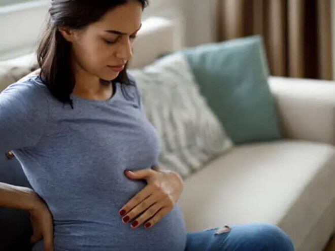 Conoce qué es la eclampsia y cuáles son sus causas. Mamá tocando el vientre y la espalda sintiendo molestia.