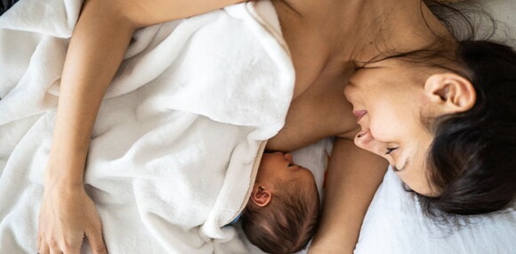 El primer mes, la leche materna pasa por muchos procesos, desde el calostro hasta la leche madura que será la definitiva y el alimento para tu bebé. Mamá acostada alimentando a su bebé recién nacido.