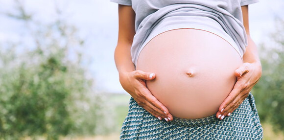 Mujer embarazada de gemelos tocándose el vientre.