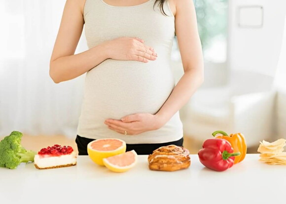 Mujer embarazada con una mesa de alimentos variados al frente