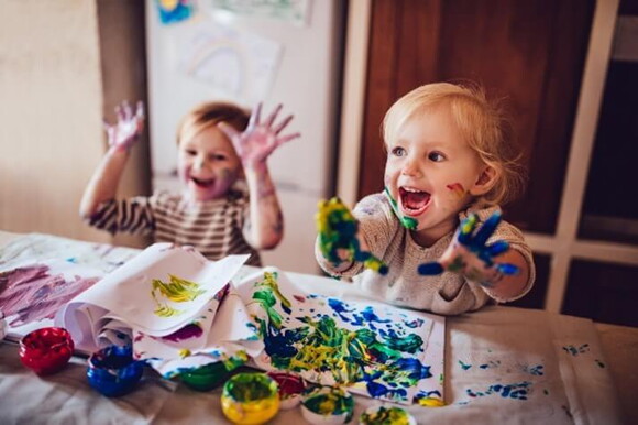 Niños pintando con pintura y riendo.